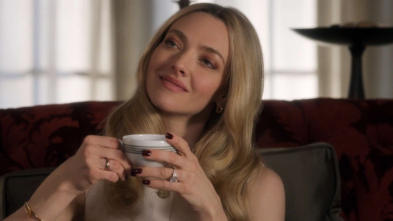 Nina Winchester smiles peacefully as she holds a tea cup while seated on a red couch in "The Housemaid"