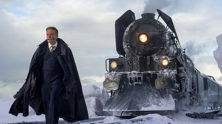 Hercule Poirot standing in front of a train in the snow in "Murder on the Orient Express."