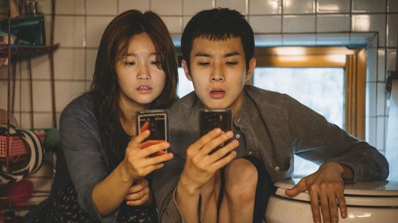 Ki-Jung and Ki-woo look at their phones in the bathroom in Parasite (2019)