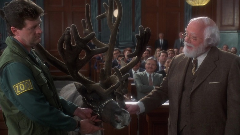 Kris Kringle stands next to a reindeer and handler in a courtroom in Miracle on 34th Street (1994)