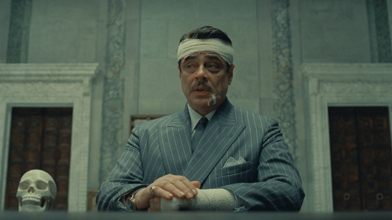 Korda standing at a ledge in a large marble room with a bandage wrapped around his head