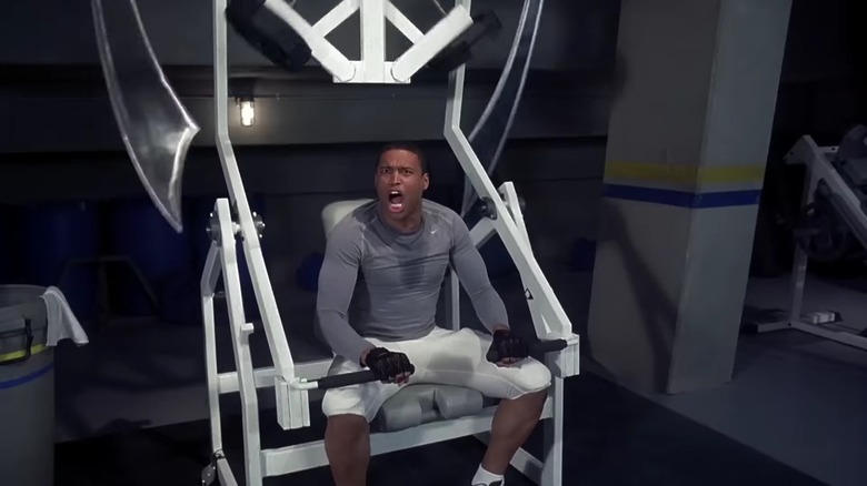 Lewis, sweaty on a gym machine with two swords dangling next to him, in "Final Destination 3" (2006)