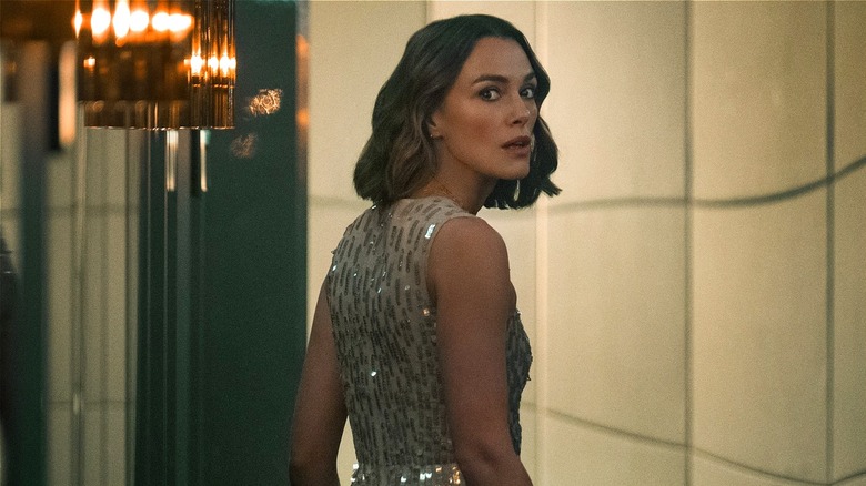 Lo looking over her shoulder in an evening gown walking down a hallway in The Woman in Cabin 10