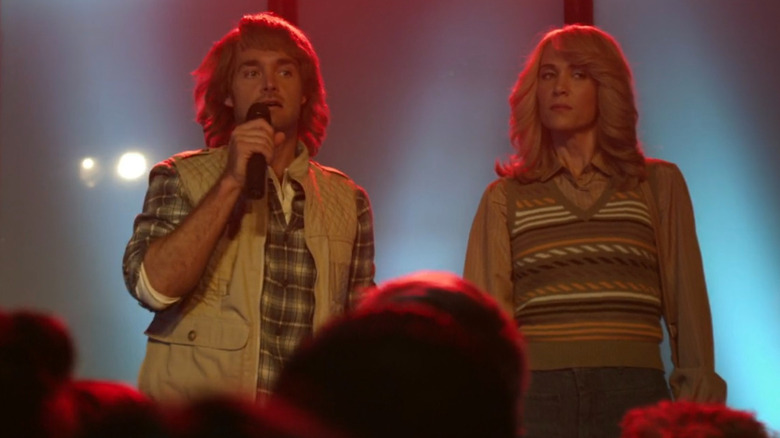 MacGruber talking into a microphone next to Vicki in "MacGruber"
