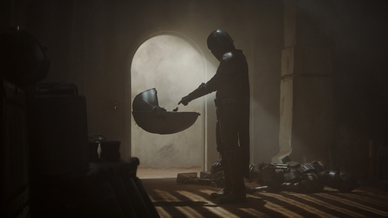 Din Djarin reaching out to touch Grogu's hand in his hover carriage in The Mandalorian (2019)