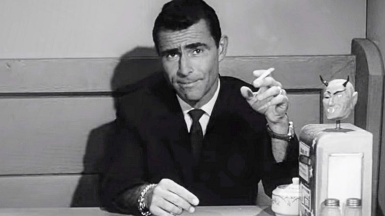 Rod Serling sitting at a desk holding a cigarette in "The Twilight Zone."