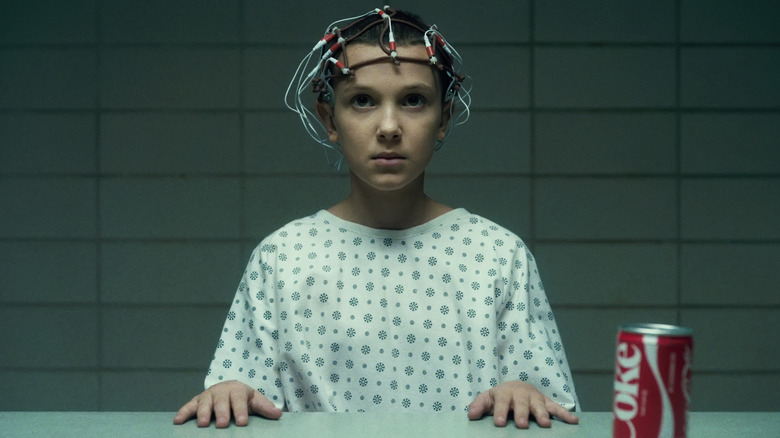 Eleven sits at table with electrodes on head in Stranger Things