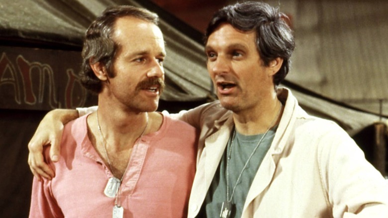 Hunnicutt and Hawkeye standing together in front of the Swamp in "M*A*S*H"