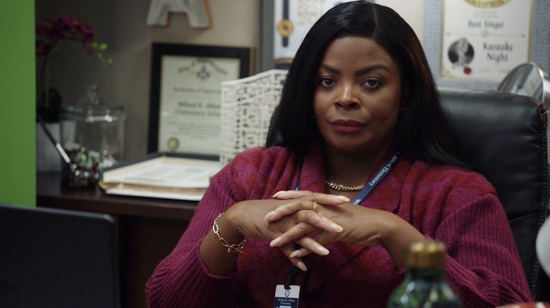 Principal Ava Coleman sitting at her desk with her hands folded in front of her, donning an unimpressed look on her face
