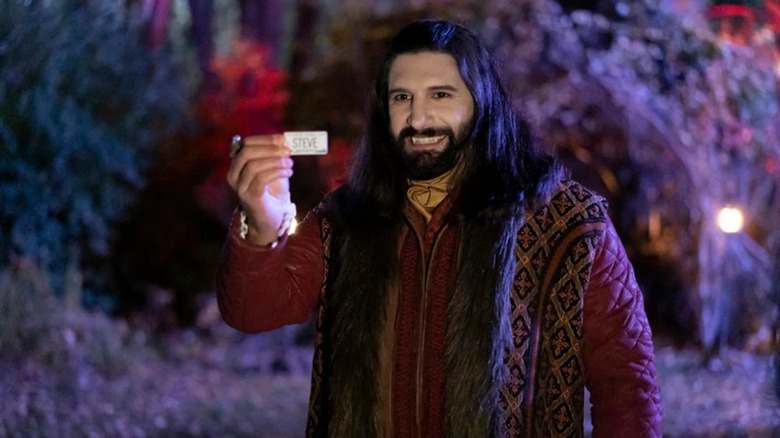 Nandor the Relentless standing outside at night, showing card in What We Do in the Shadows