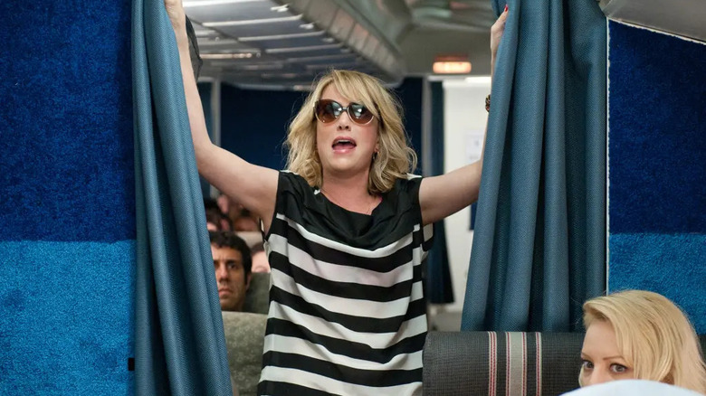 Annie opening the curtain between economy and first class with sunglasses on in Bridesmaids