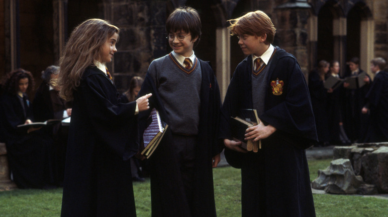 Hermione Harry and Ron in the Hogwarts courtyard talking and laughing in Harry Potter and the Sorcerer's Stone
