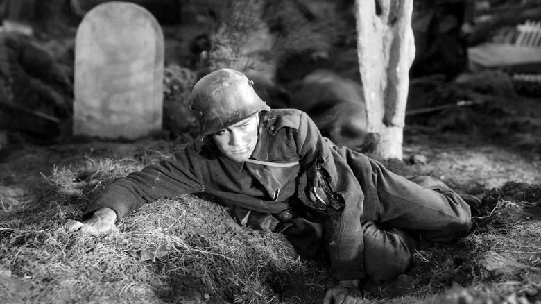Paul in uniform laying on the ground during battle in All Quiet on the Western Front