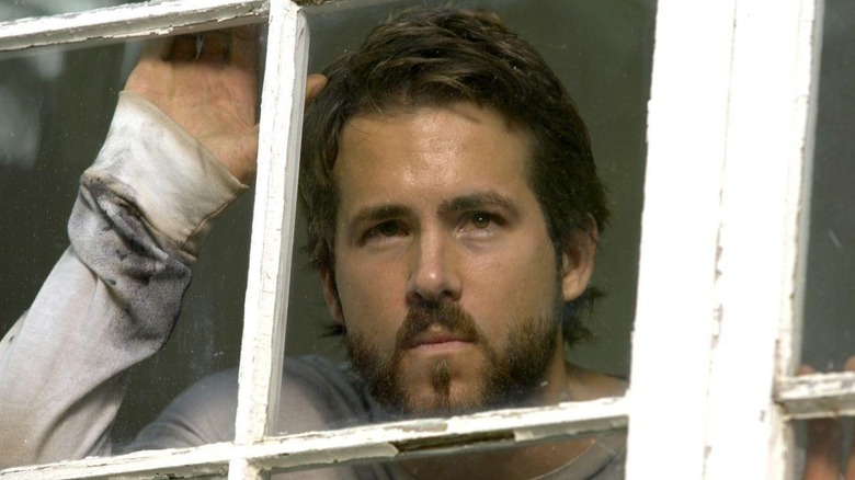 Ryan Reynolds as George Lutz looking through a window in The Amityville Horror