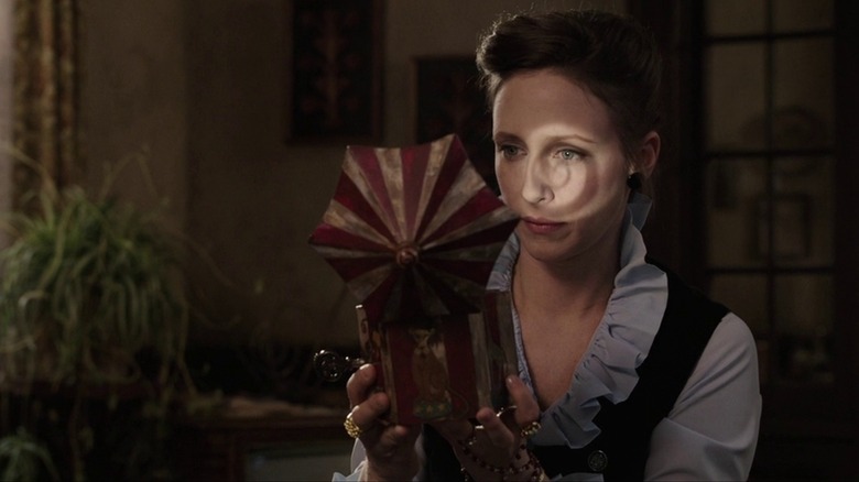 Vera Farmiga as Lorraine Warren holds a music box in The Conjuring, a spiral reflected on her face