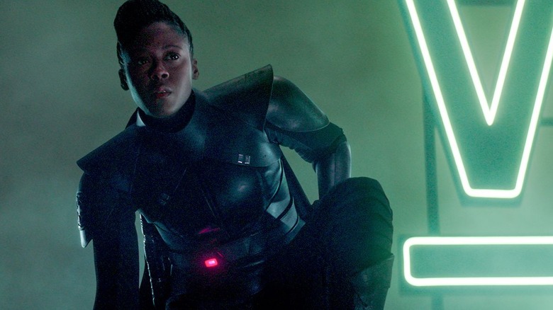 Reva crouching next to a green, neon sign