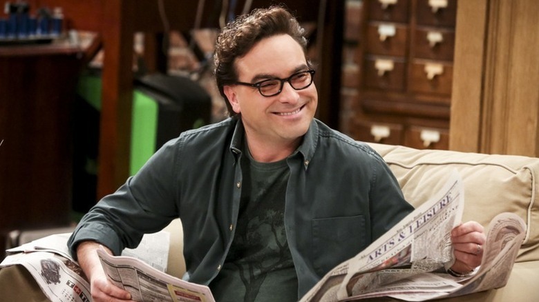 Leonard reading a newspaper on an armchair and grinning on The Big Bang Theory