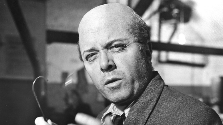 John Christie squinting while holding glasses in "10 Rillington Place"