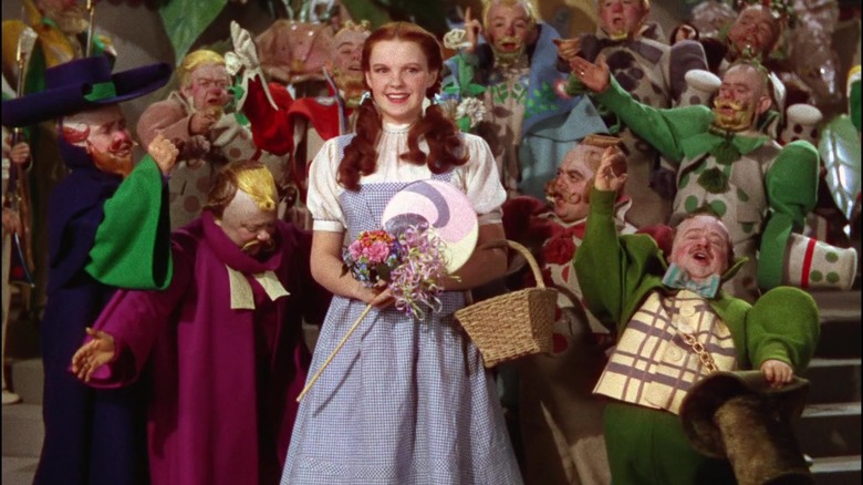 Dorothy Gale smiling in front of a crowd of munchkins in The Wizard of Oz