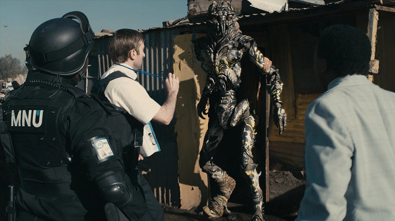 Wikus van de Merwe presents his badge to Christopher Johnson while a police officer stands behind him in "District 9"