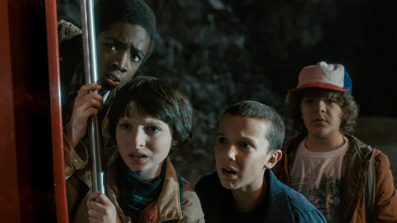 Lucas, Mike, Eleven, and Dustin hiding and peeking in Season 1 of Stranger Things