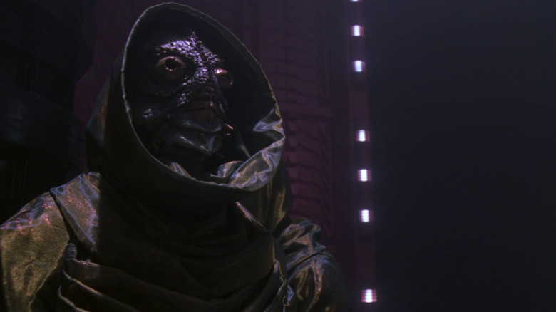An alien in a cloak stands in a dimly lit room in Star Trek: The Next Generation