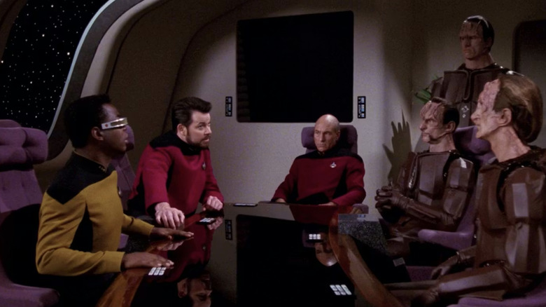 Picard, Riker, and Geordi sit at the conference table opposite three Cardassians in Star Trek: The Next Generation