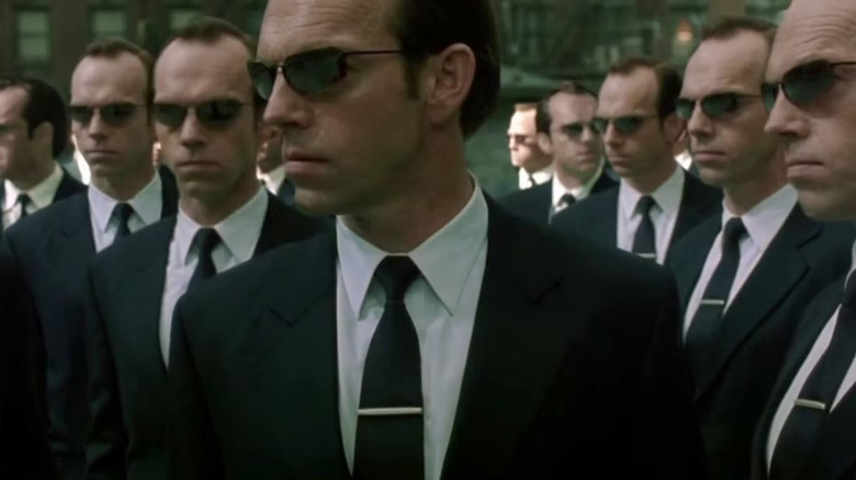 A dozen carbon copies of Agent Smith, wearing identical suits and sunglasses, stand in a crowd in "The Matrix Reloaded"