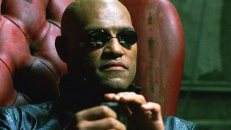 Morpheus wears black sunglasses while seated in a dirty red chair in "The Matrix"