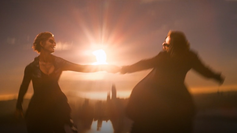 Trinity flies through the air while wearing a black leather jacket while holding Neo's hand as the sun shines behind them in "The Matrix Resurrections"