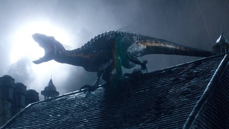 The Indoraptor howls in front of a full moon while perched on top of the roof of an old manor in "Jurassic World: Fallen Kingdom"