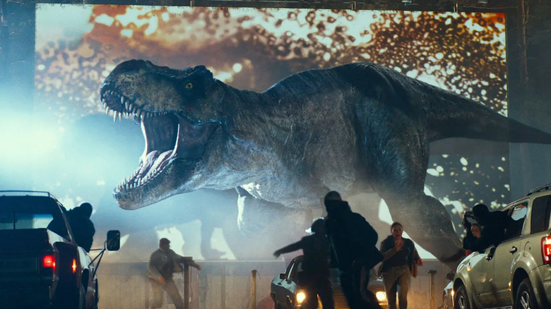 The Tyrannosaurus rex roars in front of a drive in movie theater screen as patrons run away in "Jurassic World: Dominion"