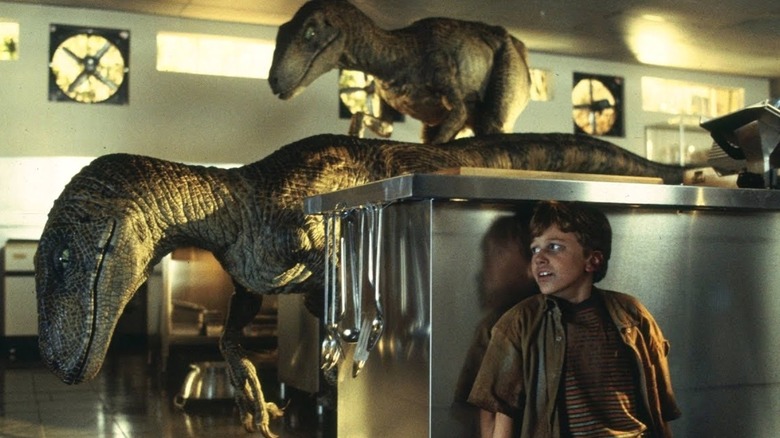 Two Velociraptors search for Tim Murphy has he hides behind a counter inside a kitchen in "Jurassic Park"
