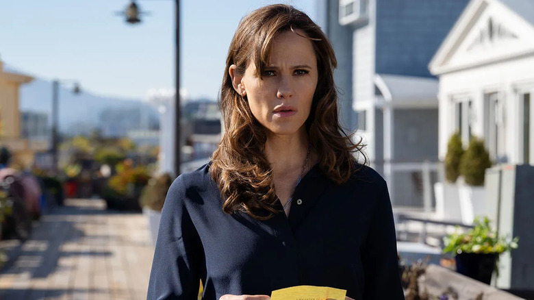 Hannah on a boardwalk holding a note and looking scared on The Last Thing He Told Me