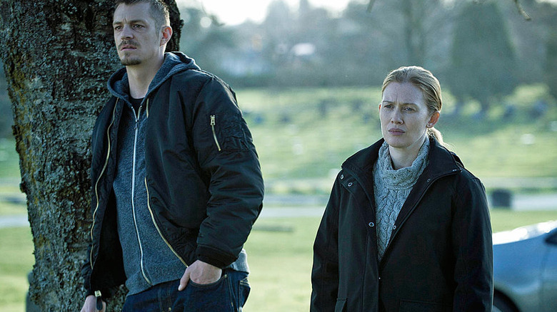 Joel Kinnaman and Mireille Enos standing next to a tree