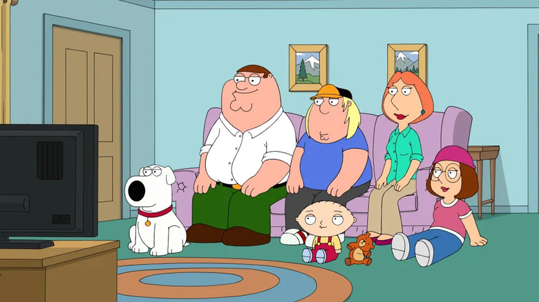 The Griffin family sit on a purple couch in front of the TV in "Family Guy"