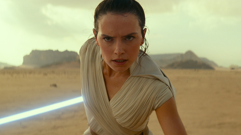 Rey grimacing in the desert with her lightsaber drawn in Star Wars: The Rise of Skywalker