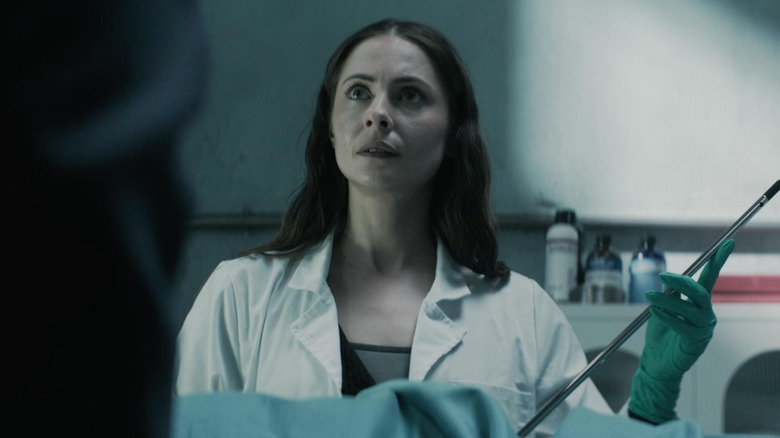 Rebecca holding a metal instrument in The Mortuary Assistant (2026)