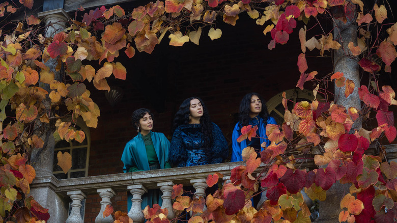 Three sisters standing on a balcony surrounded by autumn leaves in 