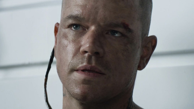 Shaved Matt Damon looks up with wire out of ear