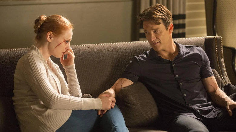 Anna Paquin as Sookie Stackhouse holds hands with Stephen Moyer as Bill Compton on a couch in True Blood.