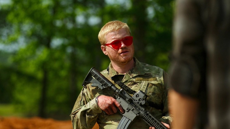 A militiaman in red sunglasses holds an automatic weapon in down position in  of Civil War (2024)