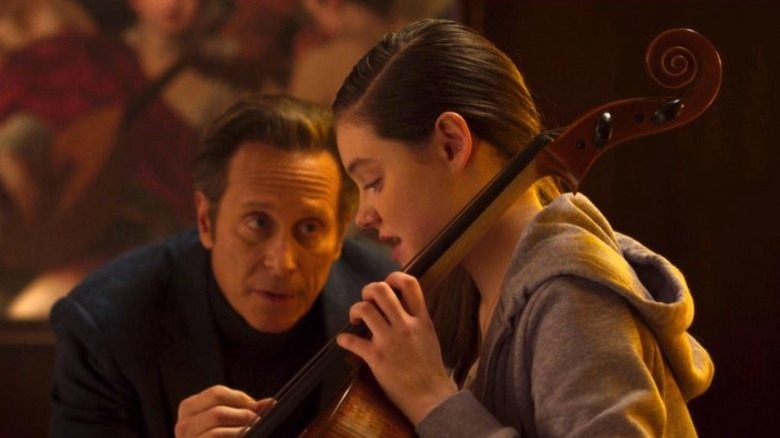 Anton leans down to give advice to Charlotte playing the cello in Perfection