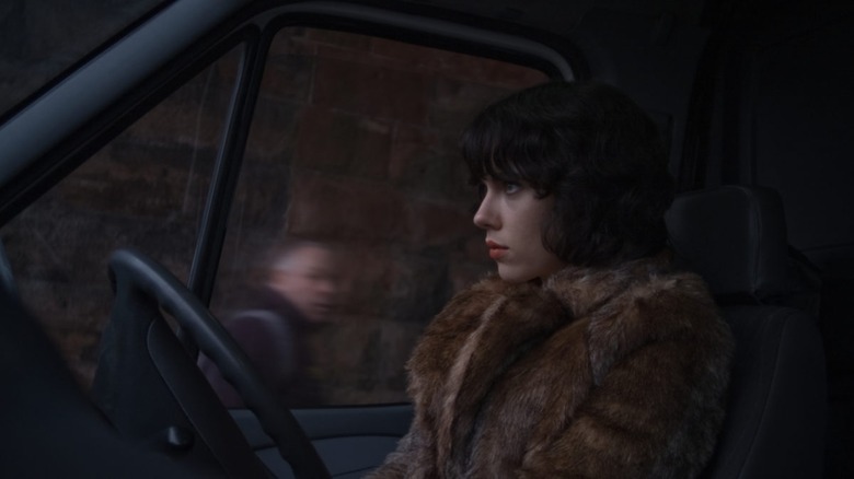 The alien woman sits in a car as people pass in Under the Skin