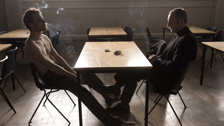 Bobby Sands sitting shirtless at table with priest in Hunger