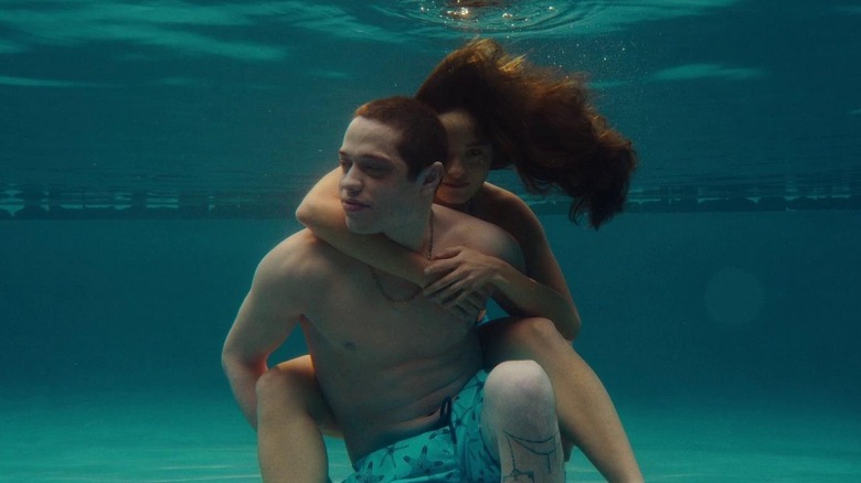 Emma (Chase Sui-Wonders) hanging onto David's (Pete Davidson) back underwater in a pool