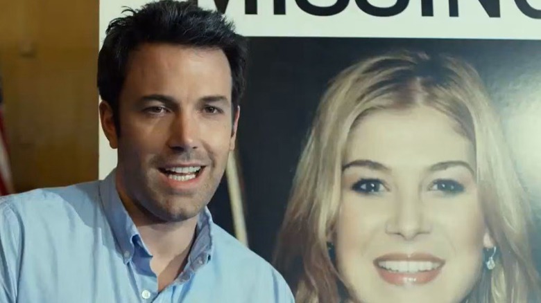 Nick smiles in front of a poster of his wife in "Gone Girl" (2014)