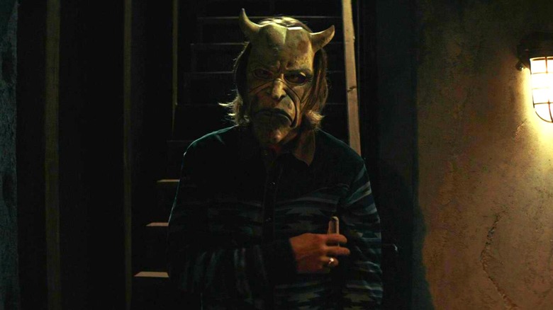 The Grabber standing at the foot of a staircase with a frowning mask in The Black Phone