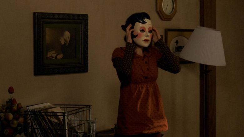 Pin-Up Girl standing by a wall with her hands on her mask in The Strangers