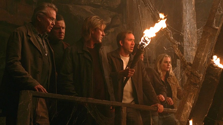 Ben and company walk through an underground passage with a torch in National Treasure (2004)